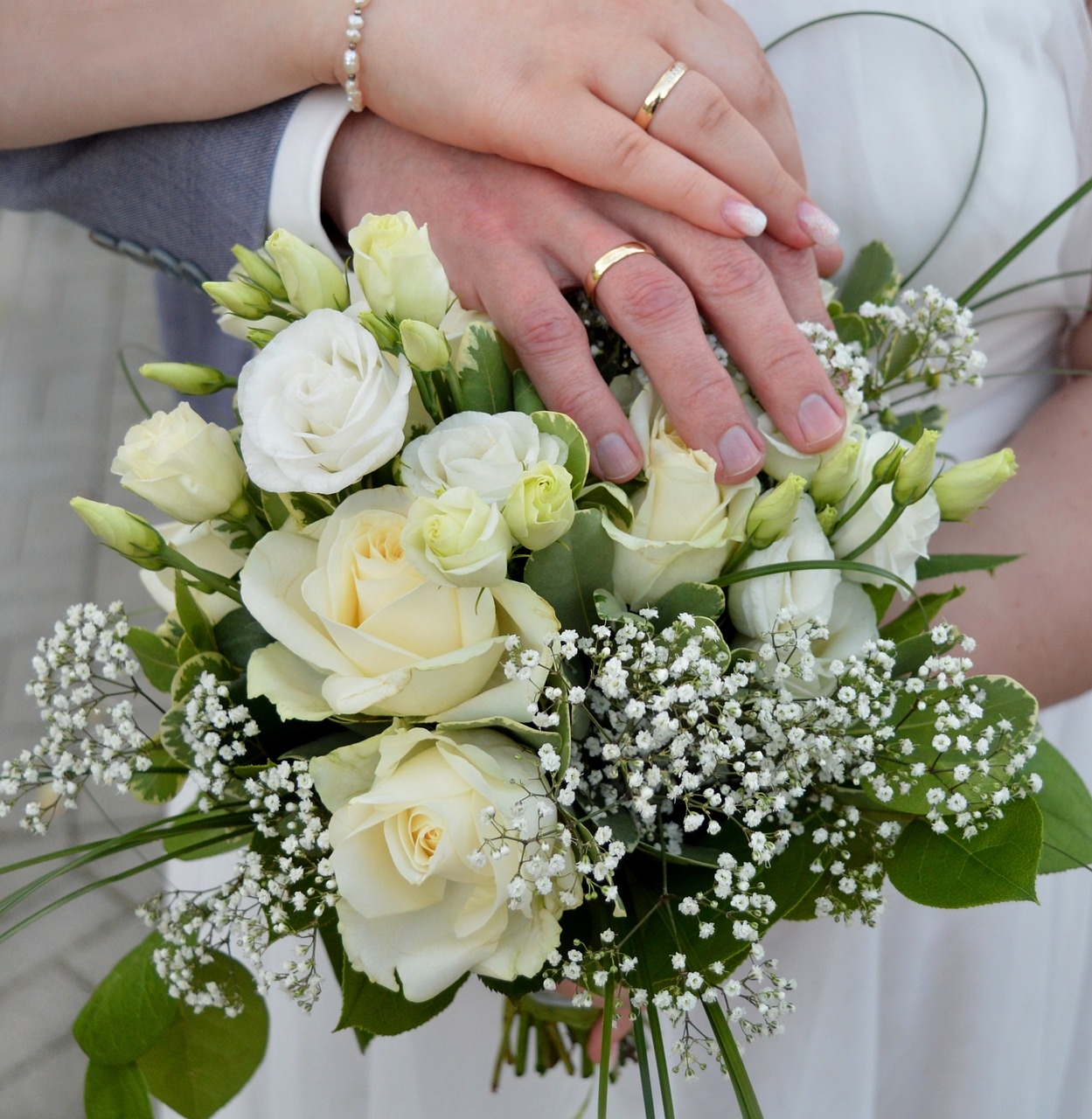 Manos de los novios sobre un ramo de rosas blancas